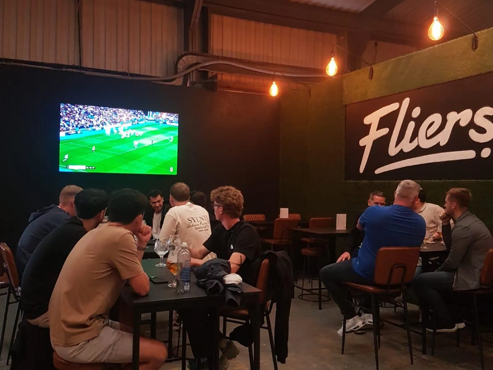 Group enjoying drinks and live sport at tables in Fliers Indoor Golf, Liverpool